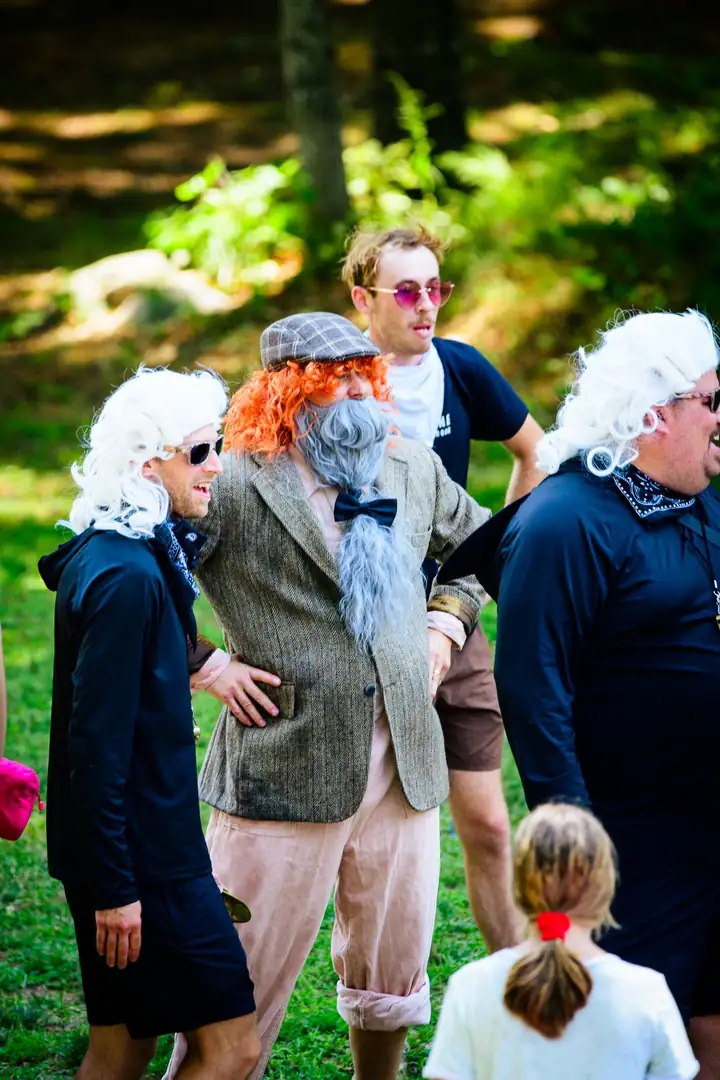 The costume crew in white and orange wigs and a tweed jacket, a little girl with pigtails in the foreground.