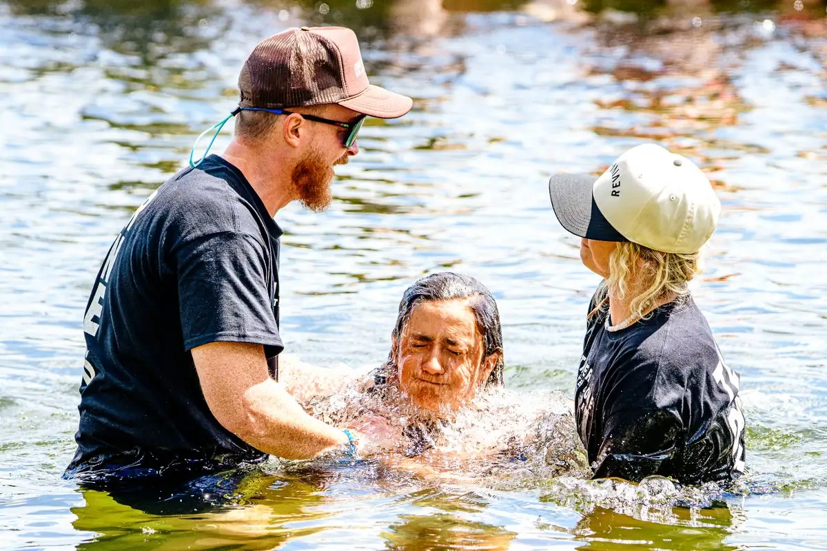 A grey-haired woman breaks the surface between the two leaders, water streaming, both of them bent over her.