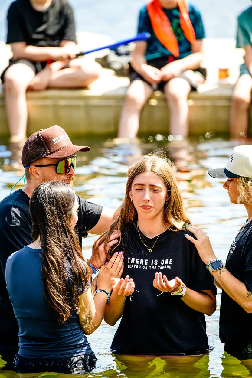 Two girls in black camp shirts standing together in the shallows, waiting their turn, THERE IS ONE readable on the shirt.