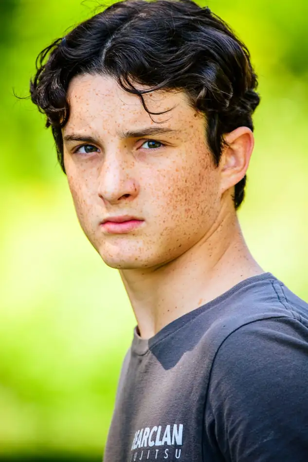 A boy in a grey tee, serious and still against a bright green background.