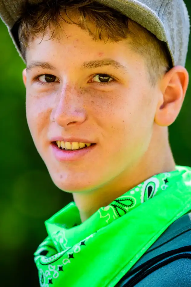A boy in a grey flat-brim cap and neon green bandana with a wide open smile.